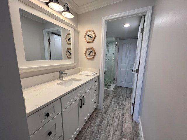 bathroom featuring hardwood / wood-style flooring, ornamental molding, a shower with shower door, and vanity