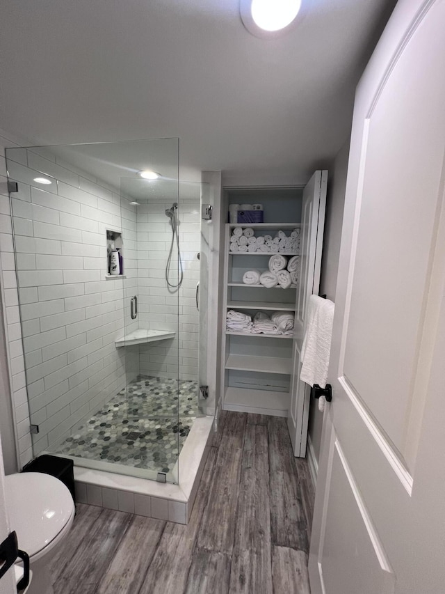 full bath featuring toilet, a stall shower, a spacious closet, and wood finished floors