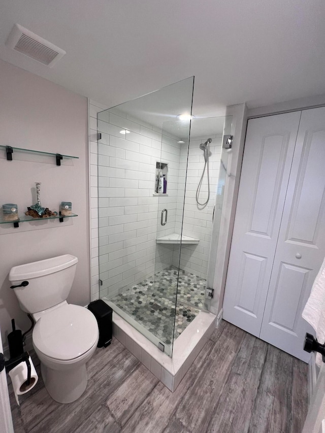 bathroom featuring wood-type flooring, toilet, and a shower with door