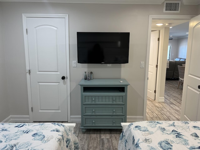 bedroom featuring baseboards, crown molding, visible vents, and wood finished floors