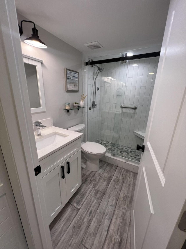 bathroom with toilet, wood finished floors, visible vents, vanity, and a shower stall