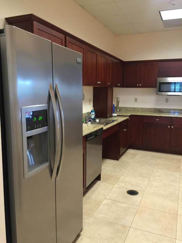 kitchen with light tile patterned floors, stainless steel appliances, a sink, dark brown cabinets, and light stone countertops