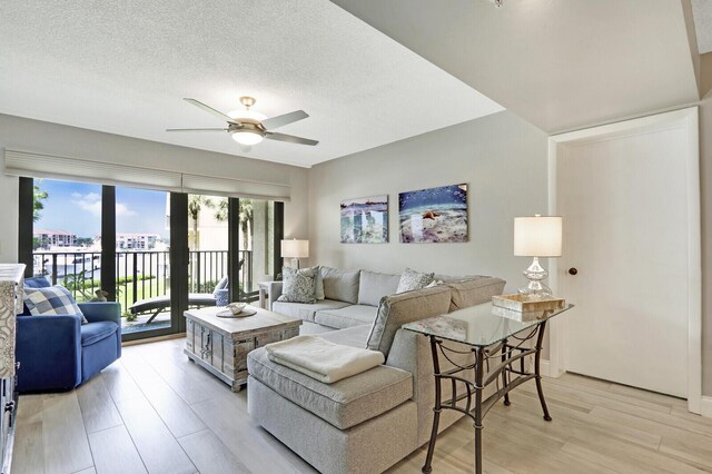 living room with ceiling fan, a textured ceiling, and light hardwood / wood-style floors