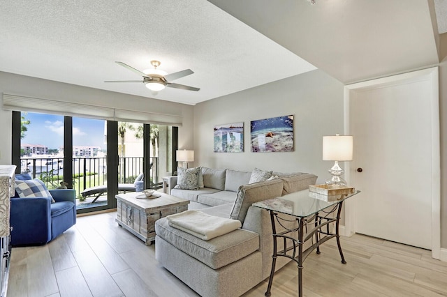 living room featuring ceiling fan, a textured ceiling, and light wood-type flooring