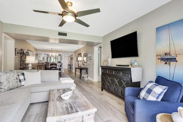 living room featuring ceiling fan with notable chandelier and light hardwood / wood-style flooring