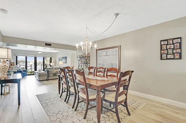 dining area with light hardwood / wood-style flooring, a textured ceiling, and a chandelier