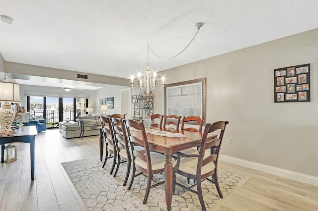 dining room featuring light wood-type flooring, a textured ceiling, and a chandelier