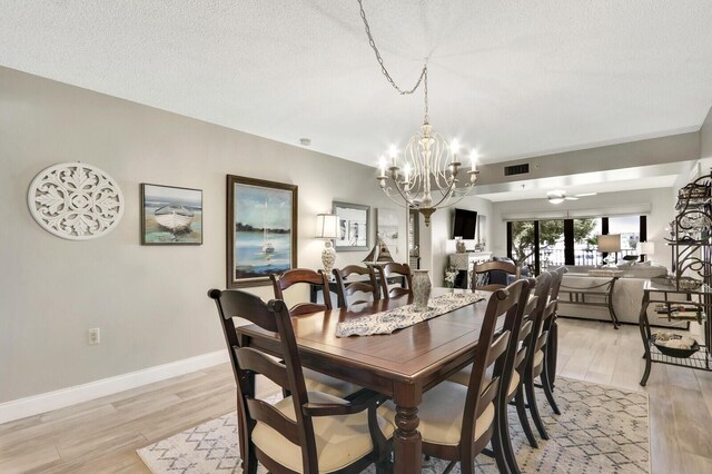 dining space with ceiling fan with notable chandelier, a textured ceiling, and light hardwood / wood-style floors