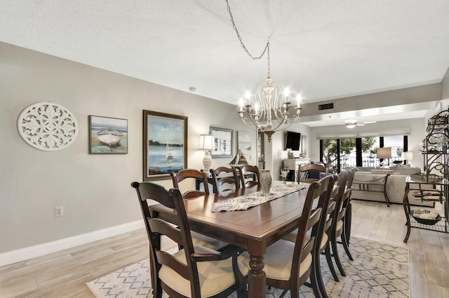 dining room with ceiling fan with notable chandelier, a textured ceiling, and light wood-type flooring