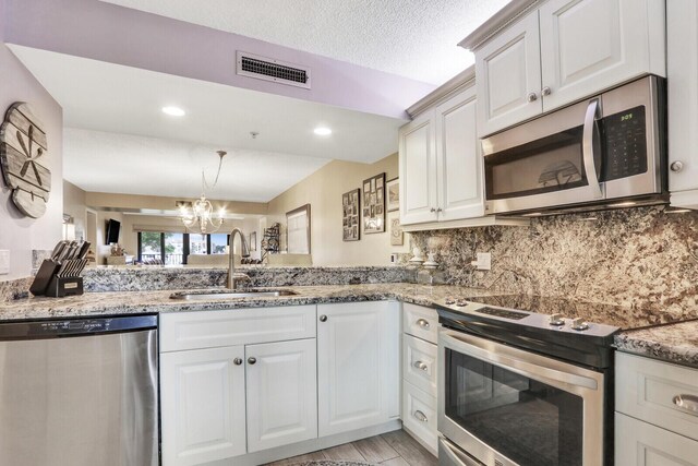 kitchen with appliances with stainless steel finishes, sink, backsplash, white cabinetry, and light stone counters