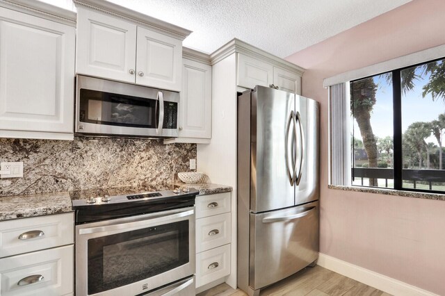 kitchen with appliances with stainless steel finishes, white cabinets, light wood-type flooring, backsplash, and light stone counters