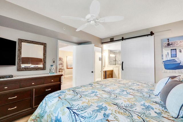 bedroom featuring ceiling fan, a barn door, light wood-type flooring, and connected bathroom