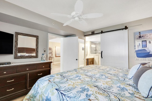 bedroom with ceiling fan, ensuite bathroom, a barn door, and light hardwood / wood-style floors