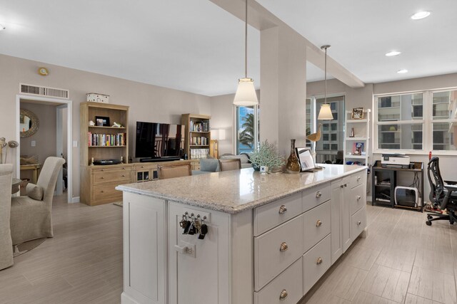 kitchen with white cabinets, a center island, pendant lighting, and light stone counters