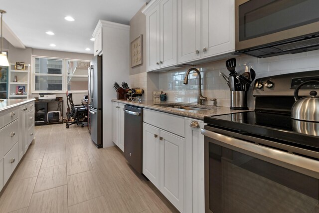 kitchen featuring white cabinetry, sink, backsplash, decorative light fixtures, and appliances with stainless steel finishes