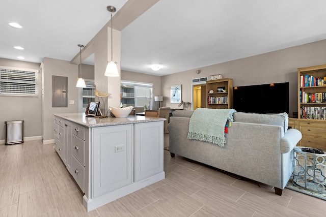 kitchen featuring a center island, electric panel, white cabinets, light stone countertops, and decorative light fixtures