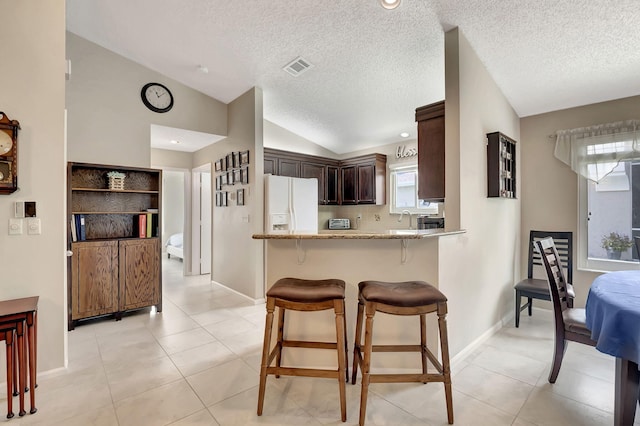 kitchen with white fridge with ice dispenser, dark brown cabinets, light tile patterned floors, kitchen peninsula, and lofted ceiling