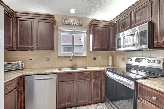 kitchen with tasteful backsplash, light stone counters, sink, a textured ceiling, and stainless steel appliances