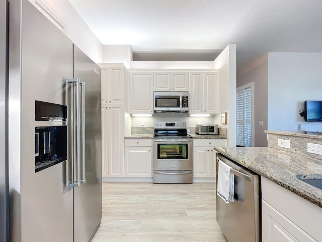 kitchen featuring stainless steel appliances, light stone counters, white cabinetry, and light hardwood / wood-style floors