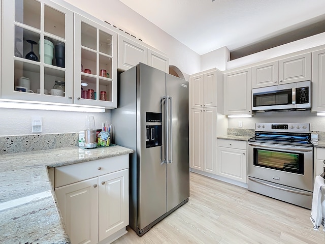 kitchen featuring appliances with stainless steel finishes, light wood-type flooring, light stone counters, and white cabinets