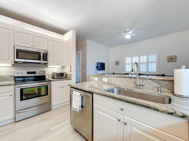 kitchen with ceiling fan, sink, stainless steel appliances, and white cabinetry