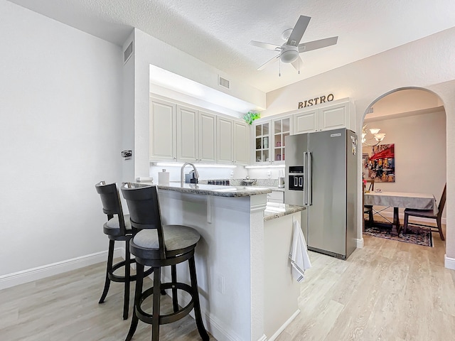 kitchen featuring high quality fridge, white cabinets, light stone countertops, and light hardwood / wood-style floors