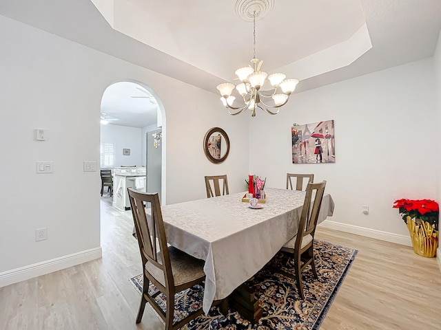 dining space with a notable chandelier, light hardwood / wood-style floors, and a tray ceiling