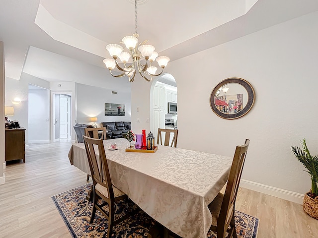 dining area featuring a notable chandelier, a tray ceiling, and light hardwood / wood-style floors