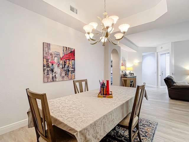 dining space with a notable chandelier, light hardwood / wood-style floors, and a tray ceiling