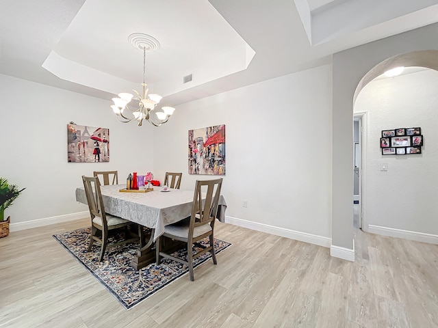 dining room with light wood-type flooring, a raised ceiling, and a chandelier