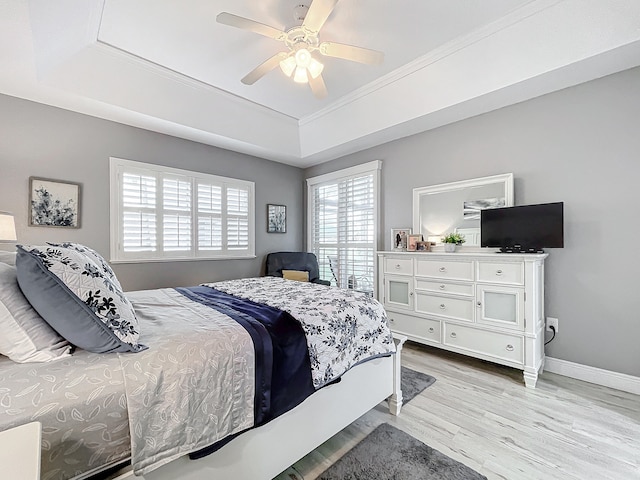 bedroom with ceiling fan, a raised ceiling, light wood-type flooring, and multiple windows