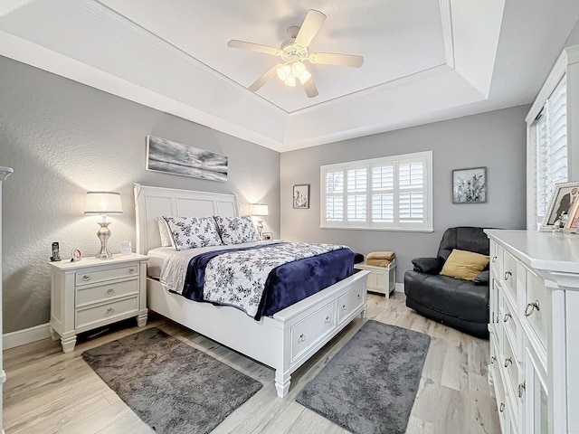 bedroom with ceiling fan, light wood-type flooring, and a tray ceiling