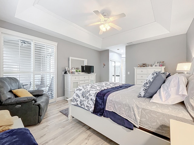 bedroom featuring ceiling fan, light hardwood / wood-style floors, multiple windows, and a raised ceiling