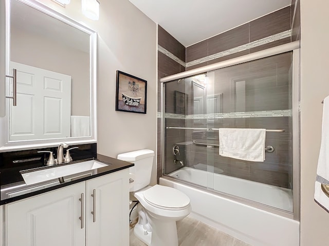 full bathroom with toilet, wood-type flooring, vanity, and bath / shower combo with glass door