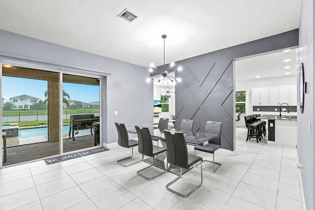 tiled dining area featuring a textured ceiling, a healthy amount of sunlight, sink, and a chandelier