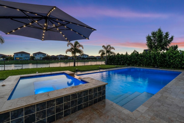 pool at dusk featuring an in ground hot tub and a water view