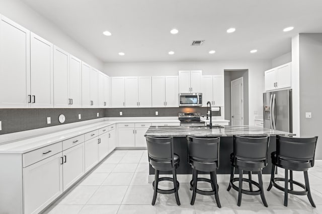 kitchen featuring appliances with stainless steel finishes, white cabinetry, sink, a breakfast bar area, and a center island with sink