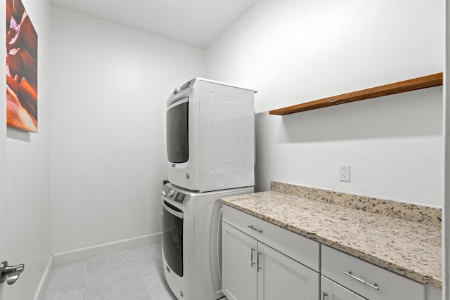 clothes washing area with light tile patterned floors, stacked washer and clothes dryer, and cabinets