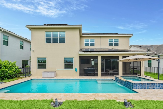 rear view of property featuring a swimming pool with hot tub, a patio, and solar panels