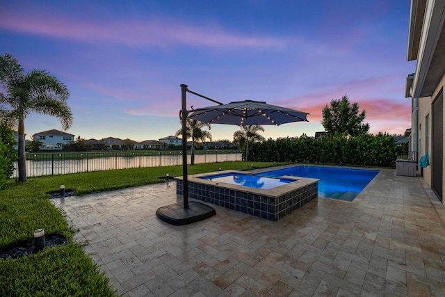 pool at dusk featuring an in ground hot tub and a patio