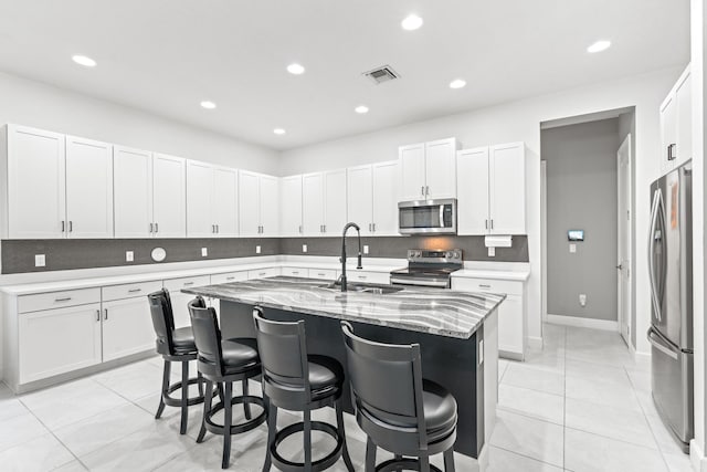 kitchen with a kitchen island with sink, sink, light stone countertops, a breakfast bar, and appliances with stainless steel finishes