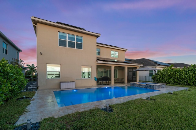 back house at dusk with a yard, a patio, and a pool with hot tub