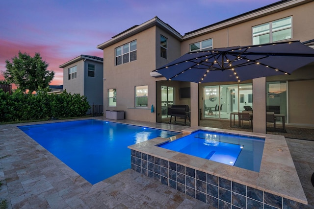 pool at dusk with an in ground hot tub and a patio