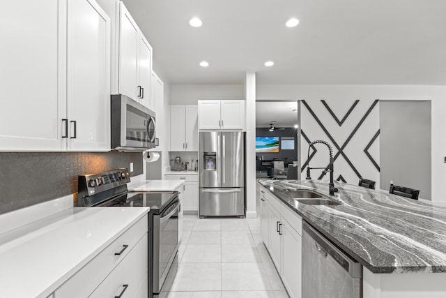 kitchen with backsplash, light tile patterned floors, appliances with stainless steel finishes, white cabinetry, and sink