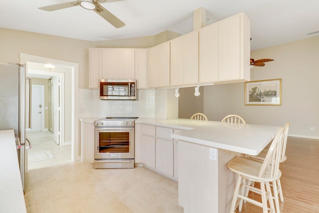 kitchen featuring stainless steel appliances, light wood-type flooring, a kitchen bar, ceiling fan, and tasteful backsplash