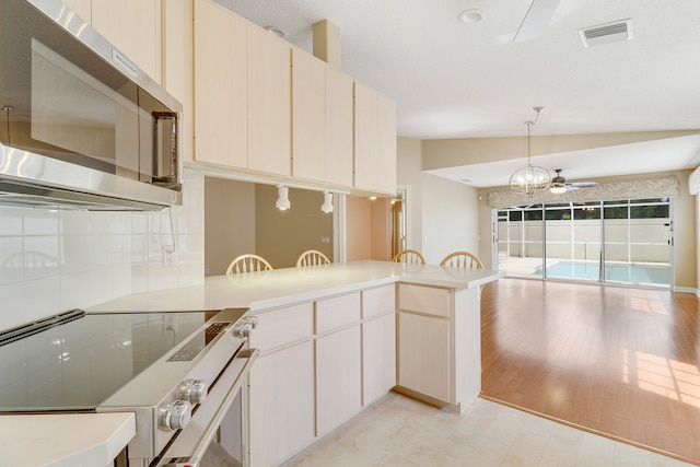 kitchen featuring light wood-type flooring, ceiling fan with notable chandelier, lofted ceiling, range with electric stovetop, and kitchen peninsula