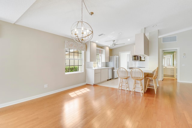 kitchen featuring lofted ceiling, ceiling fan with notable chandelier, appliances with stainless steel finishes, light wood-type flooring, and white cabinetry