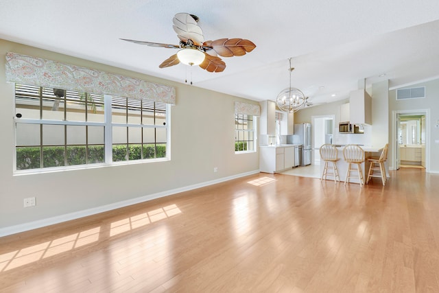 unfurnished living room with lofted ceiling, light wood-type flooring, and ceiling fan with notable chandelier