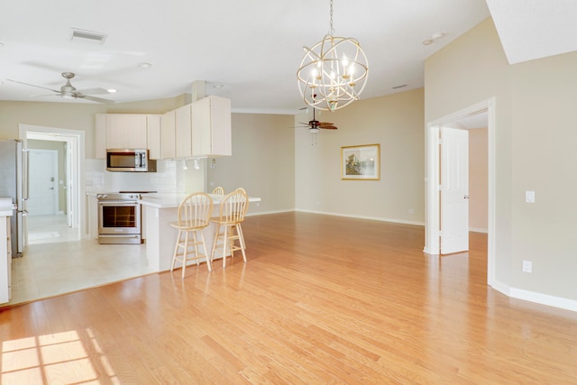 kitchen with ceiling fan with notable chandelier, white cabinetry, appliances with stainless steel finishes, light tile patterned floors, and backsplash