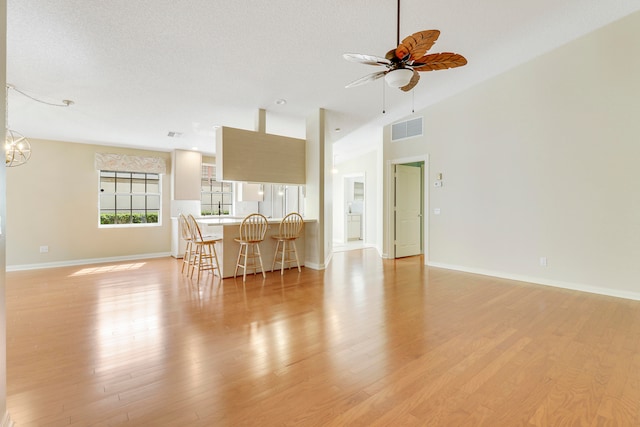 living room with ceiling fan, high vaulted ceiling, a textured ceiling, and light hardwood / wood-style floors